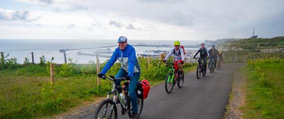 Cyclists riding along a path with the port of Dover in the background.