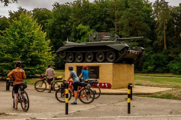 Cyclists looking at a tank on a memorial plinth. 